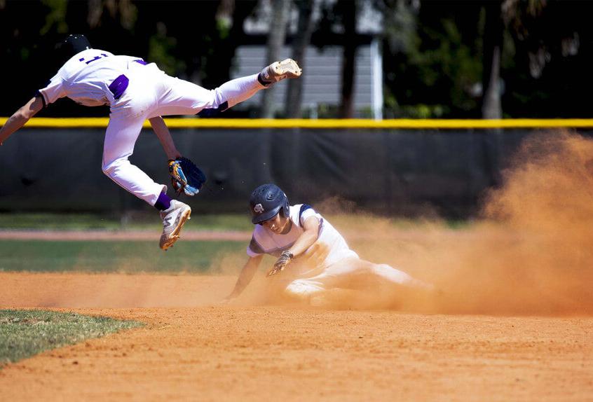 保利预科 棒球 athlete sliding into base as the opposing team member leaps in the air for the ball